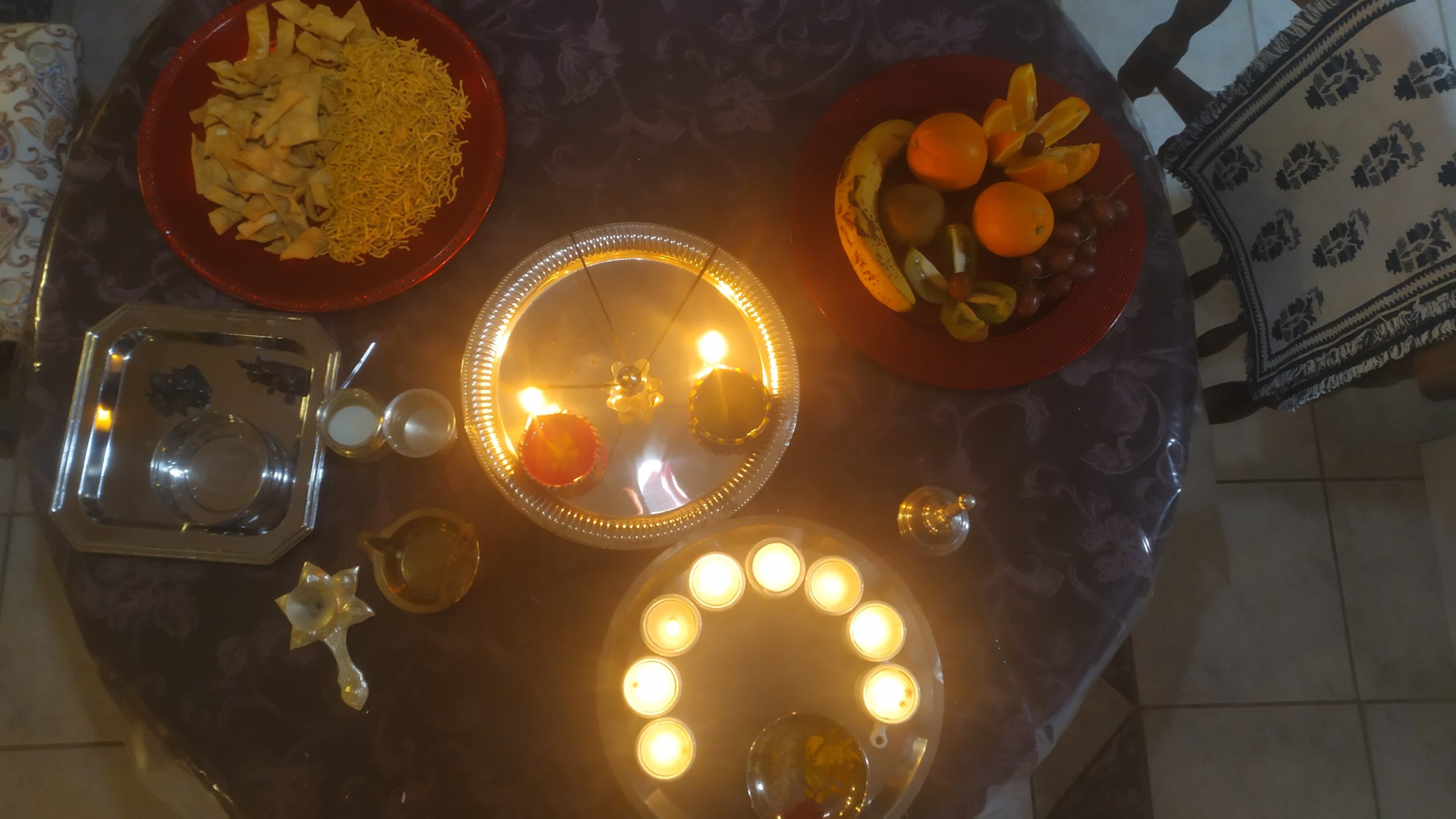 une vue du haut d'une table sur laquelle sont déposés confieseries, encens, bougies, fruits et statuettes de Dieu