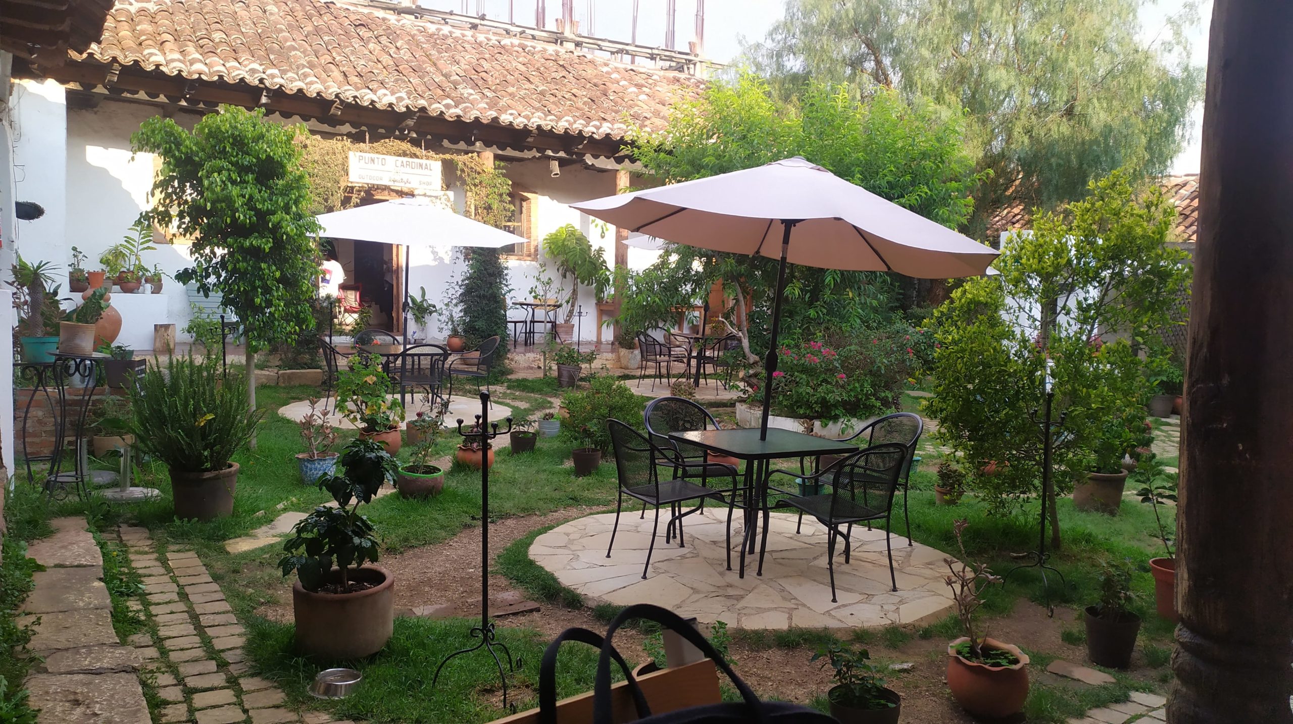 une terrasse dans un jardin avec des tables et des parasols. Le soleil est de sortie pour une fois